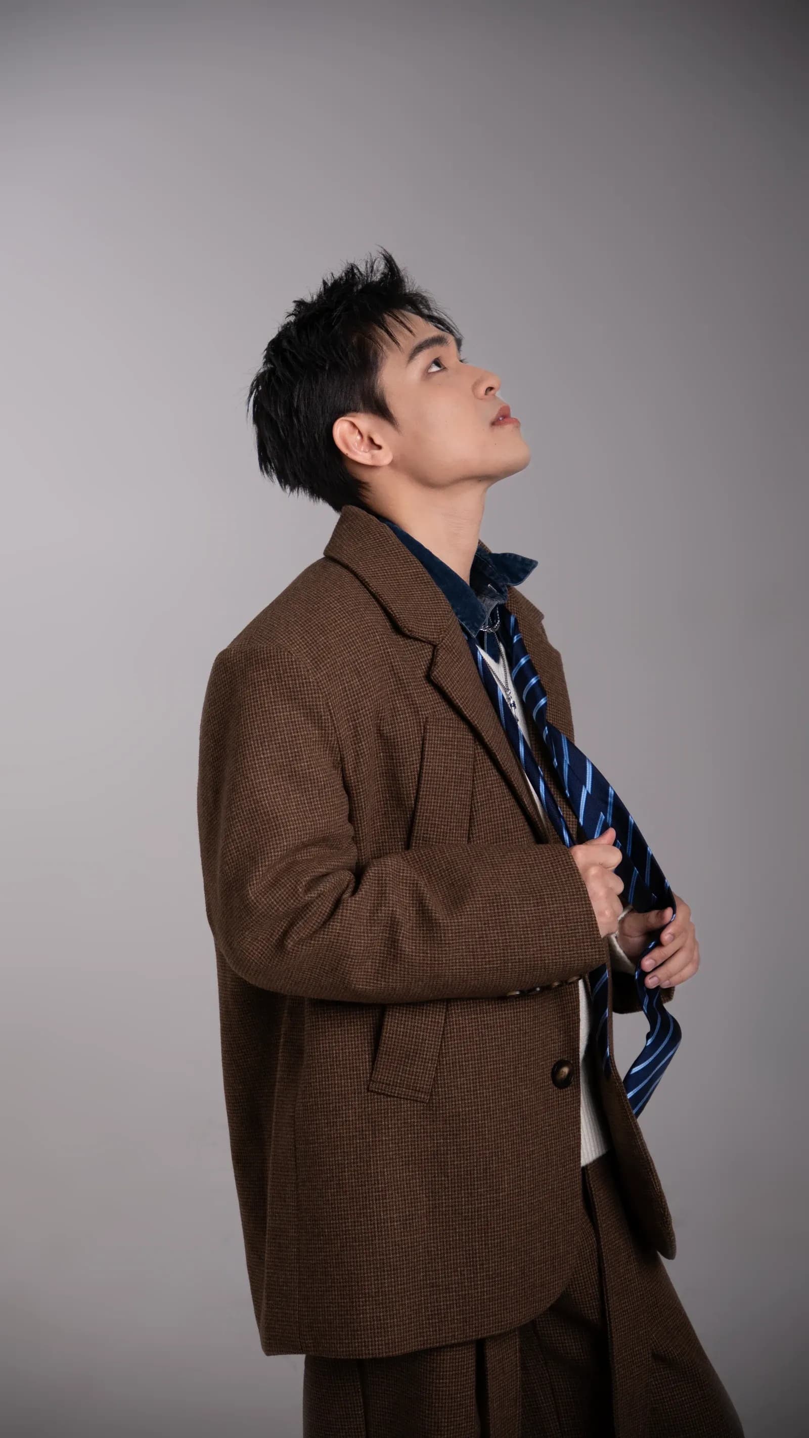 Kien Pham looking upward in a brown jacket against a grey studio background